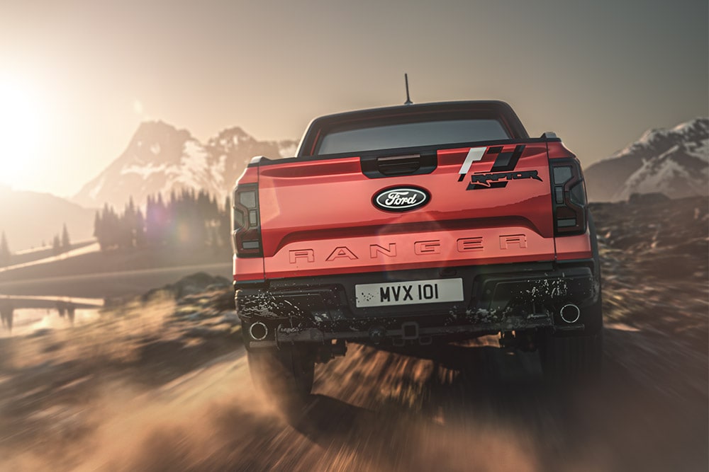 Rød Ford Ranger Raptor sett bakfra på en grusvei med fjell i bakgrunnen.