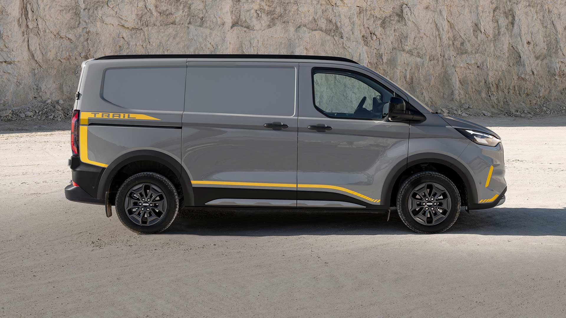 Grå Ford Transit Custom Trail-varebil med gule detaljer, vist fra siden.