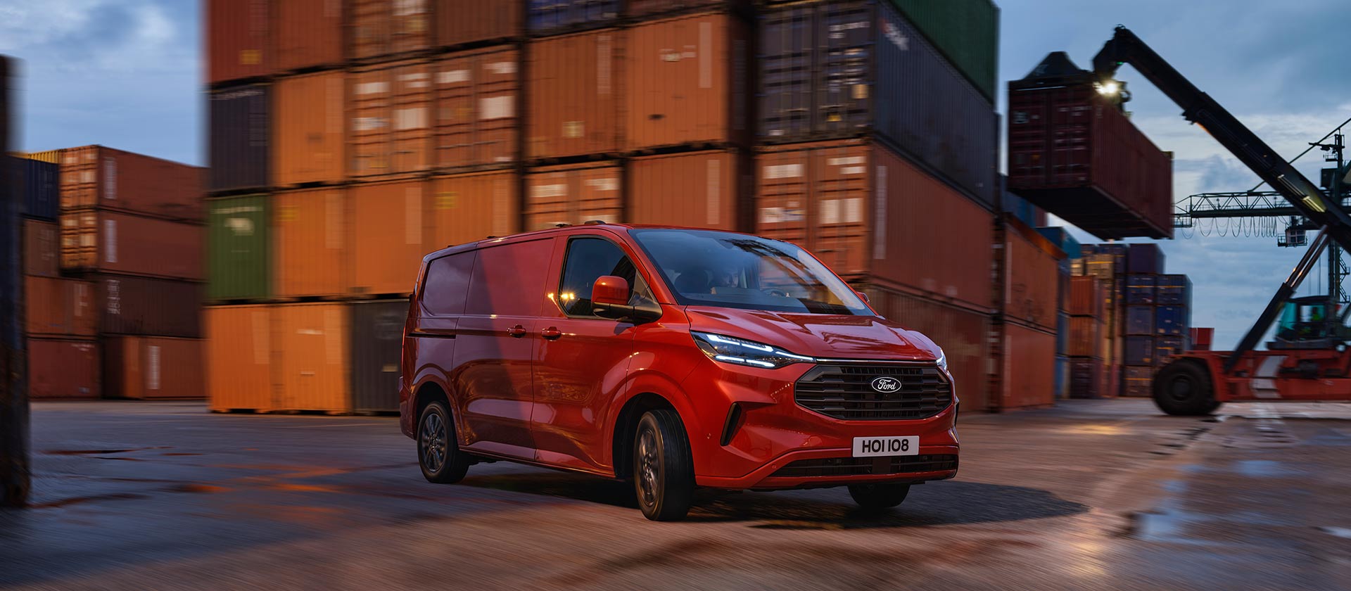 Rød Ford Transit Custom-varebil kjører gjennom et kaiområde.