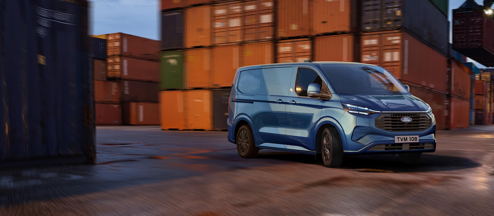 Blå Ford Transit Custom ladbar hybrid kjører gjennom et skipsverft.