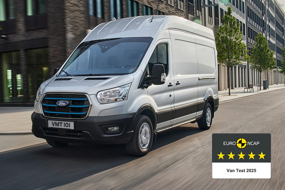Sølvfarget Ford E-Transit elektrisk varebil som kjører på en vei med et "Gold 2022 Commercial Van Safety"-merke.