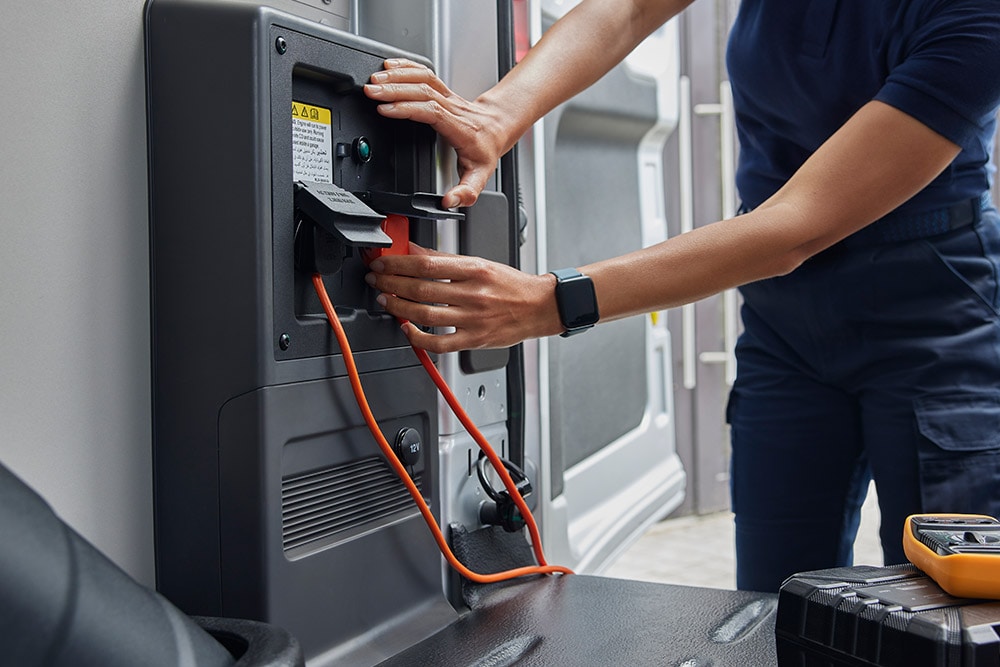 Nærbilde av en person som kobler en ladekabel til en Ford E-Transit elektrisk varebil.