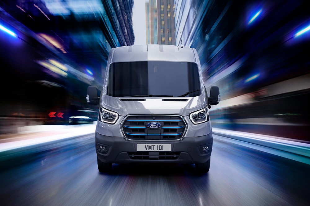 Mørk grå Ford E-Transit elektrisk varebil som kjører på en vei.