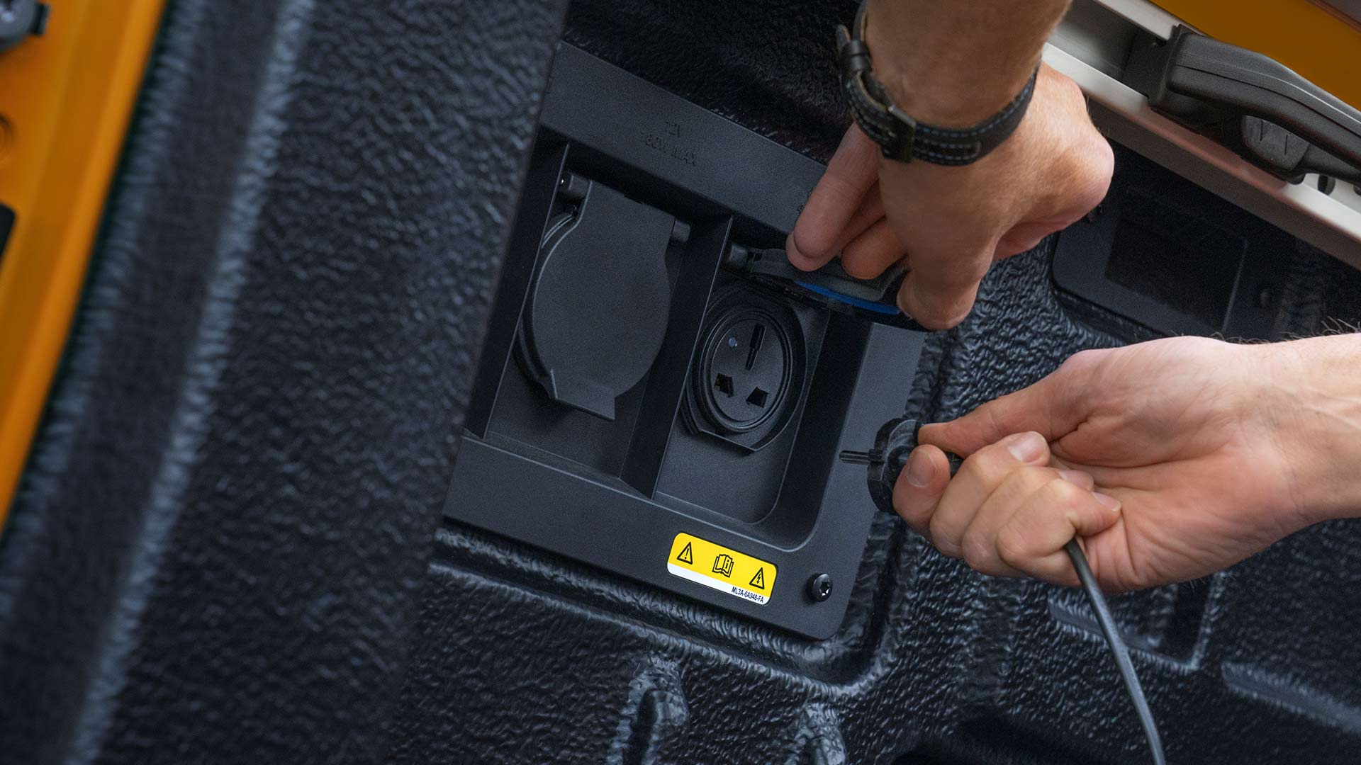 Nærbilde av hender som kobler kabler til strømuttaket på lasteplanet til Ford Ranger.