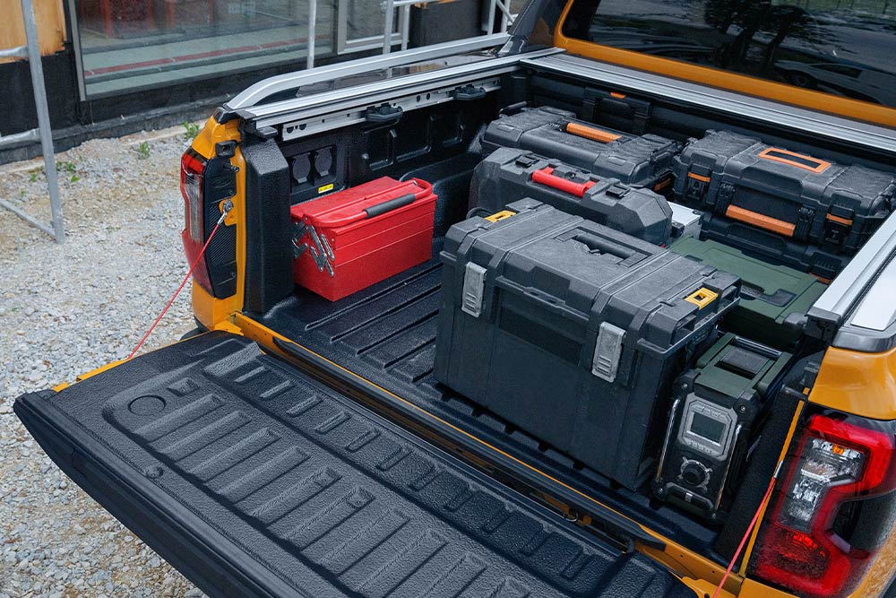 Bakdøren på en gul Ford Ranger er nede, med en treplanke festet til den ved hjelp av en klemme.