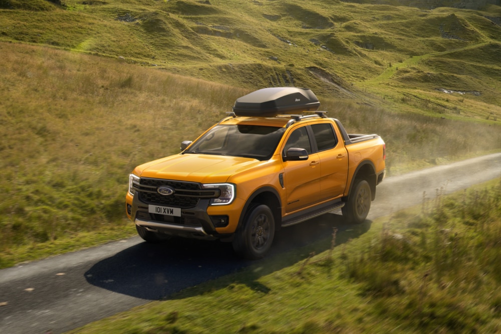 Gul Ford Ranger kjører på en landevei med takboks montert på taktstativ. 