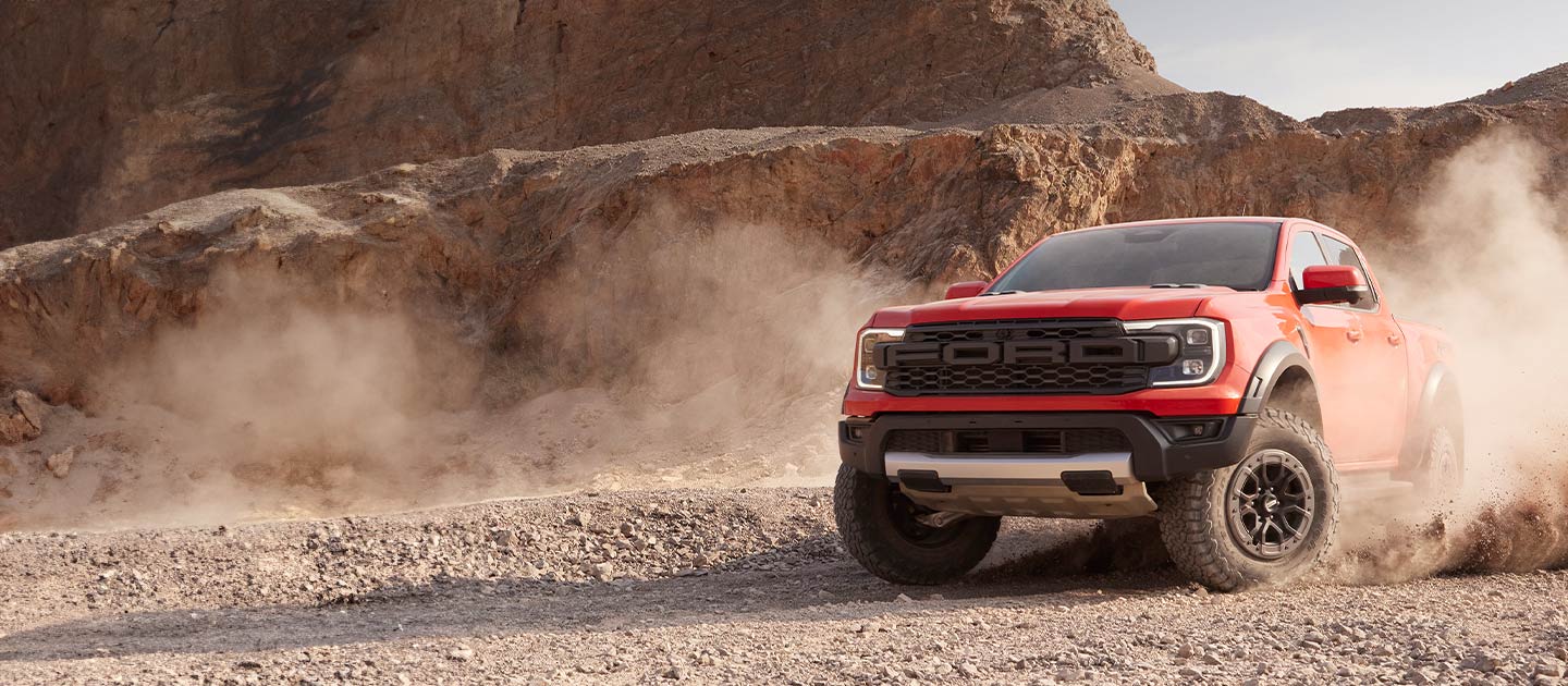 En rød Ford Ranger Raptor virvler opp støv mens den kjører gjennom et ørkenlandskap.