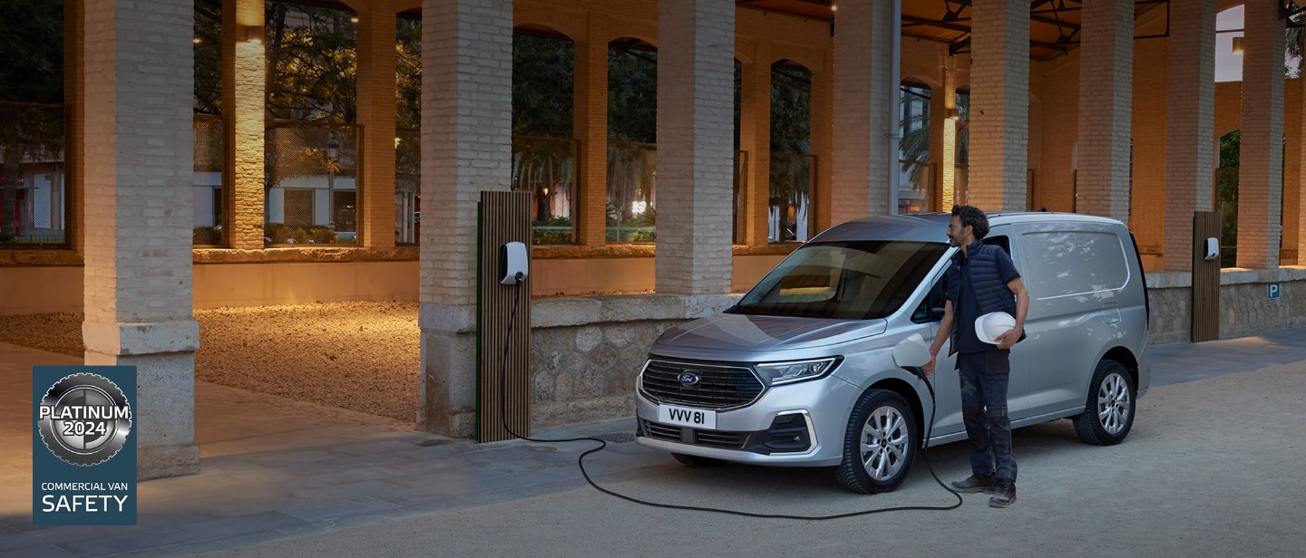 En mann som holder en vernehjelm plugger en ladekabel fra veggboks inn i splitter nye Ford Transit Connect i Stardust Silver.