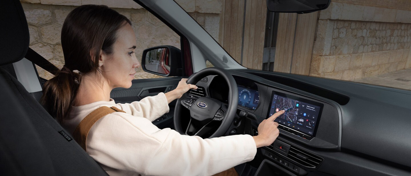 En kvinne berører den 10-tommers touchskjermen mens hun sitter i førersetet på helt nye Ford Transit Connect.