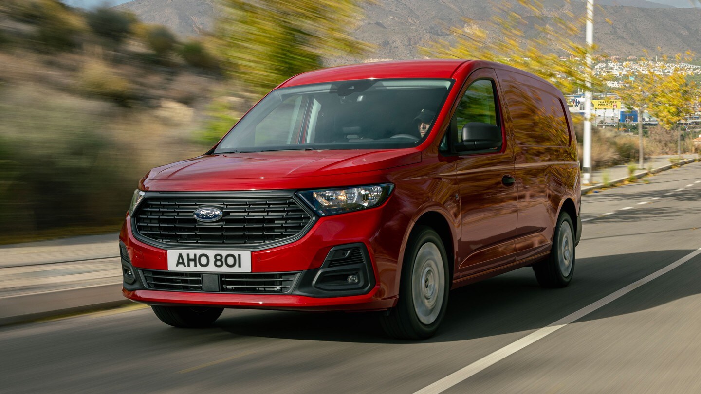 Visning av frontgrill og frontlykter på splitter nye Ford Transit Connect i Maple Red som kjører langs en vei. 