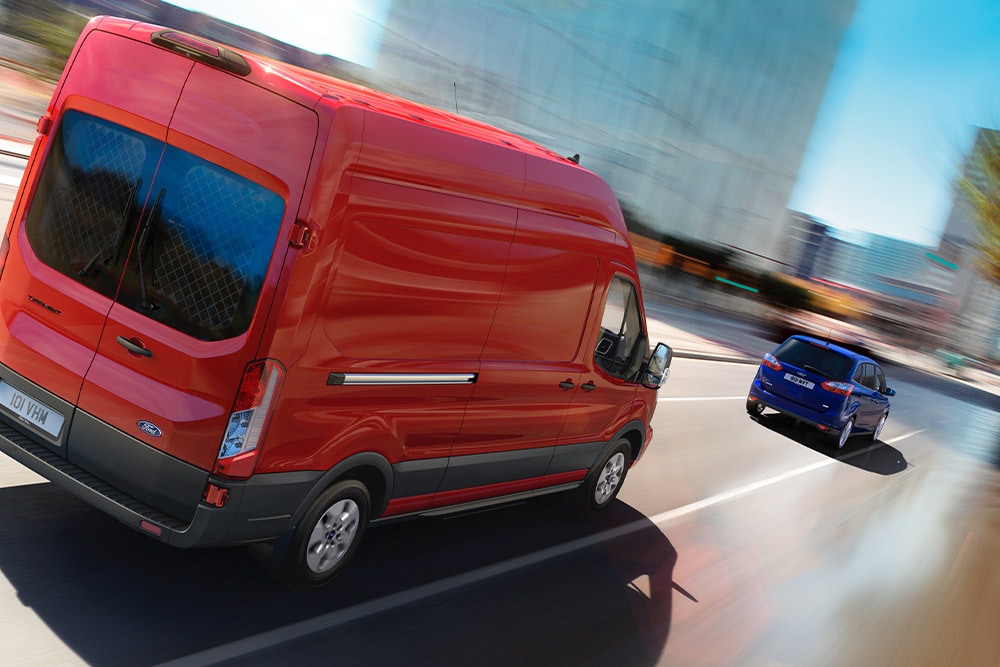 Rød Ford Transit-varebil som kjører på en vei.