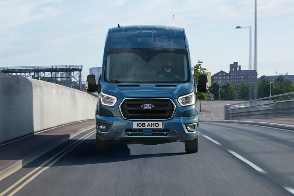 Visning forfra av en blå Ford Transit varebil som kjører på en vei. 