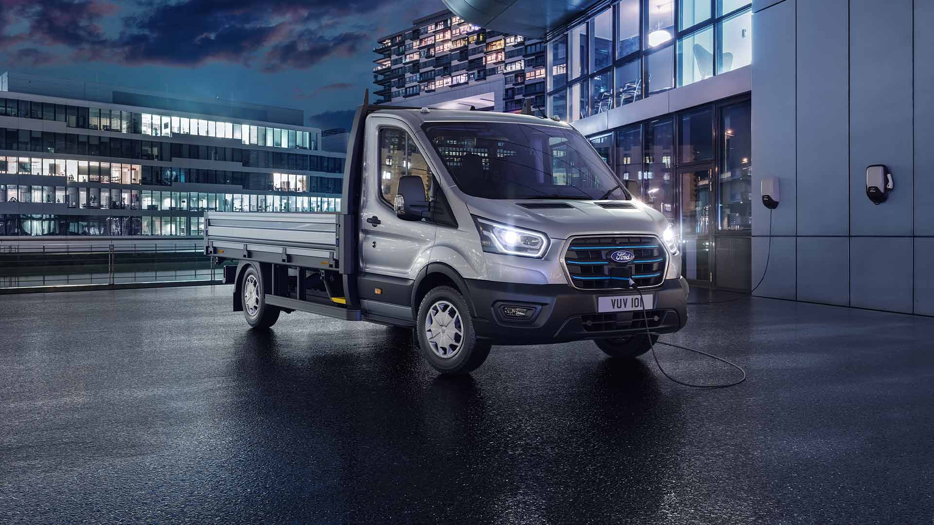 Sølvfarget Ford Transit Chassis Cab parkert foran en moderne bygning om natten.