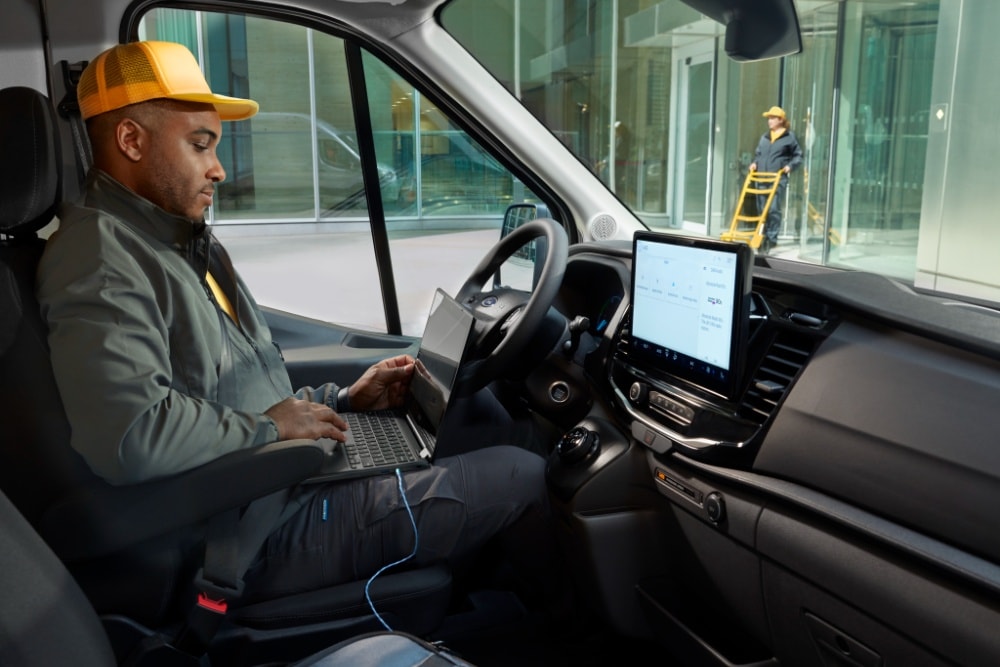 En mann som sitter i førersetet i en Ford Transit-varebil og bruker en laptop.