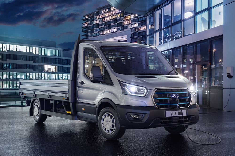 Sølvfarget Ford E-Transit Chassis Cab parkert foran en moderne bygning om natten.