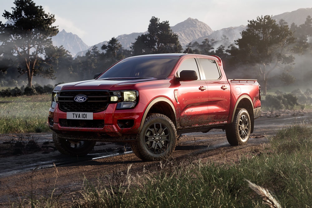En rød Ford Ranger Raptor som kjører på en grusvei gjennom et naturskjønt landskap.