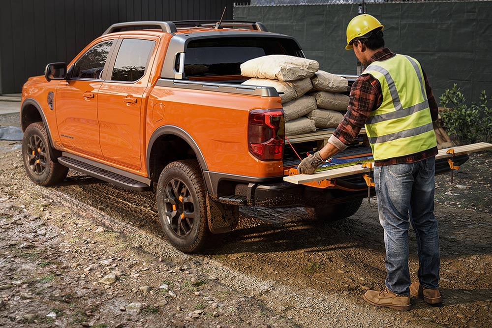 En anleggsarbeider som laster utstyr på lasteplanet til en oransje Ford Ranger.