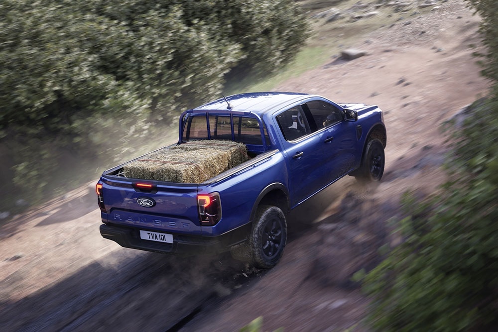 Visning bakfra av en blå Ford Ranger som kjører langs en grusvei.