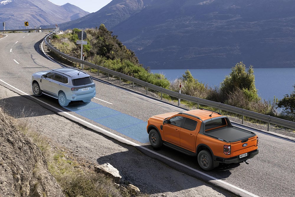 En oransje Ford Ranger bruker det avanserte systemet for førerassistanse langs en motorvei ved kysten.