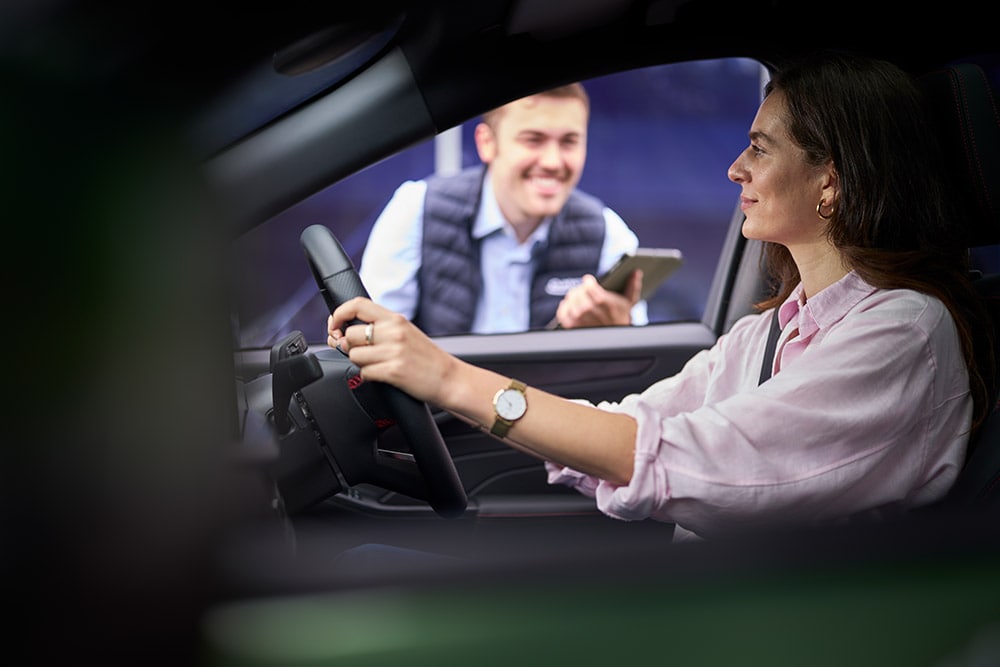 En person i førersetet av en Ford-bil, som ser på en tekniker som holder et nettbrett utenfor.