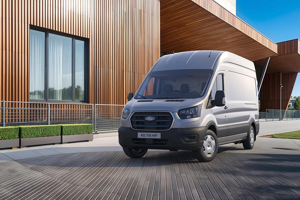 En grå Ford E-Transit varebil er parkert utenfor en moderne bygning med treaksenter.