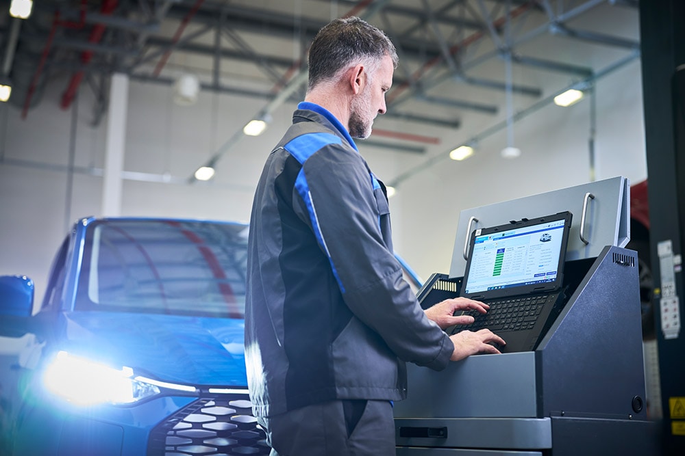 En tekniker som arbeider på en laptop koblet til en blå Ford SUV på et serviceverksted.