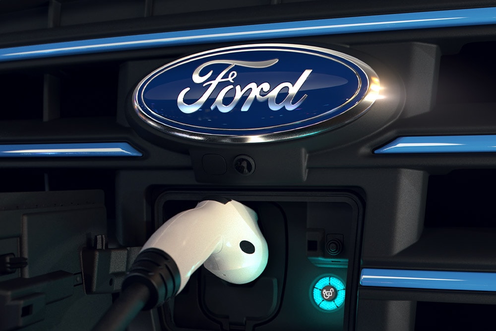 Nærbilde av en hvit ladekabel plugget inn i den fremre ladeporten på et elkjøretøy fra Ford.