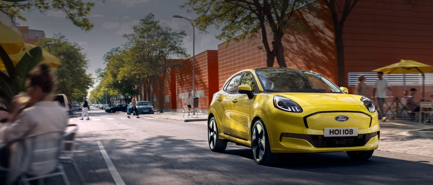 En gul elektrisk Ford Puma® som kjører langs en bygate vist forfra.