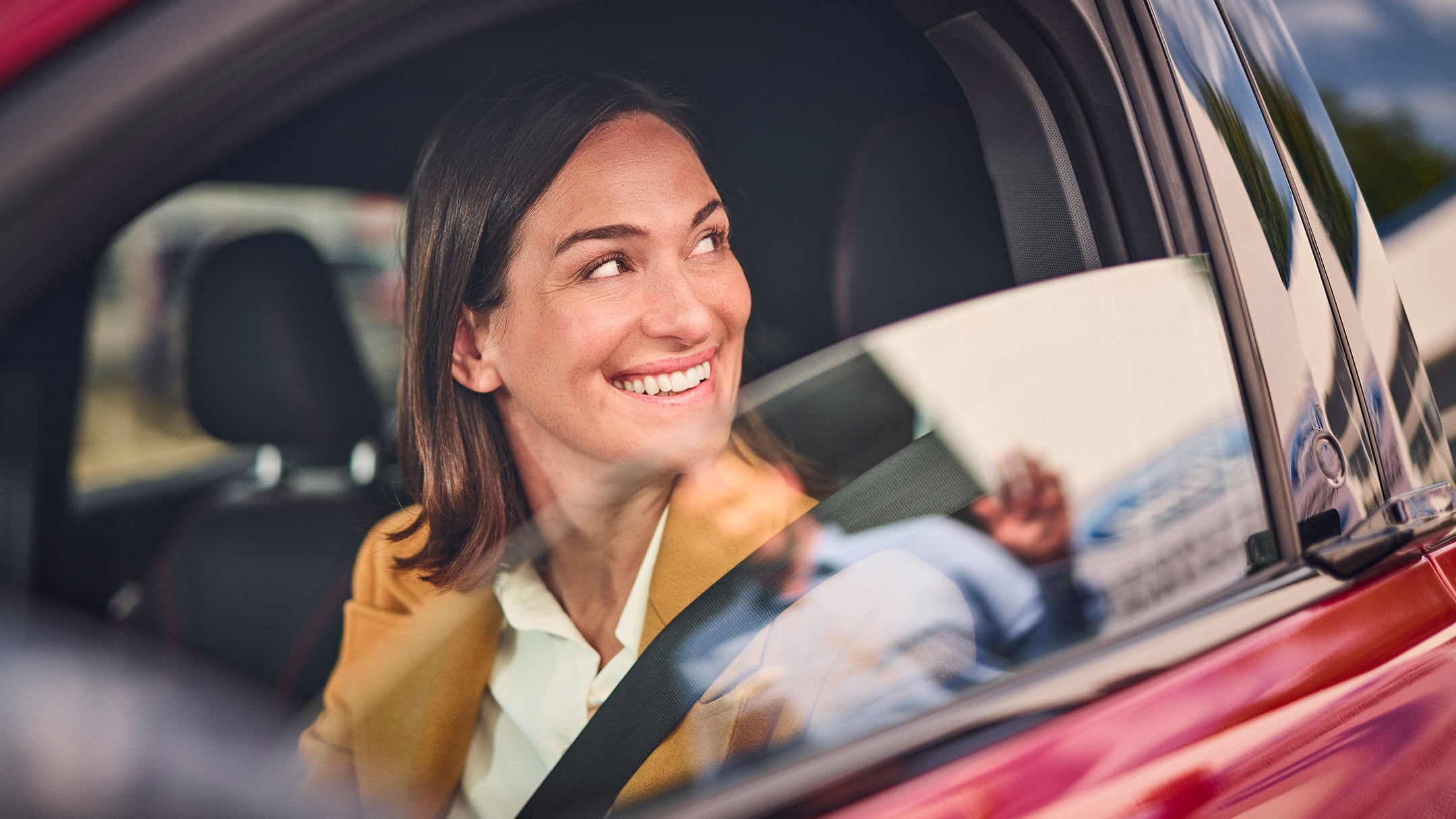 En person som sitter i en rød Ford og smiler
