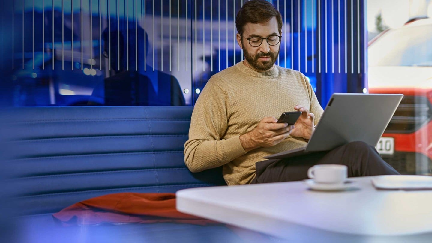 En person som sitter på en kontorpult med en laptop og en smarttelefon, i et moderne kontorlandskap. 
