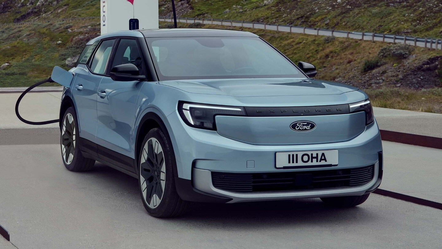 Lyseblå Ford Explorer Electric kjører på en grusvei og virvler opp støv, sett fra siden.
