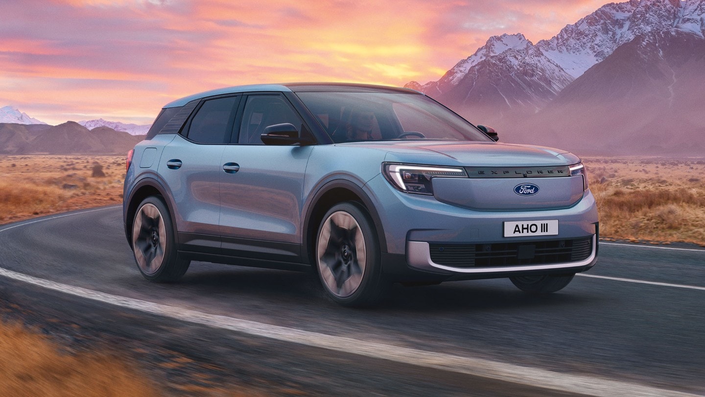 Trekvart forfra av en lyseblå Ford Explorer Electric som kjører på en vei i solnedgangen.