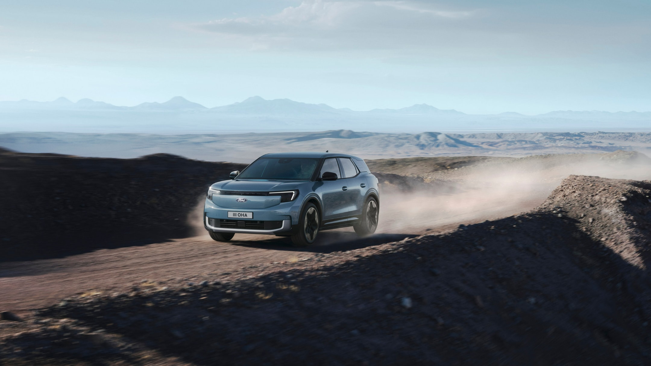 Lyseblå Ford Explorer Electric lader på en ladestasjon, sett fra siden.
